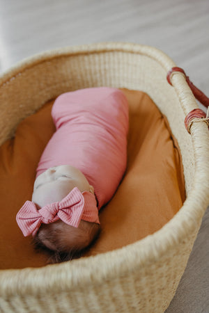 baby covered with pink blanket in brown woven basket with brown